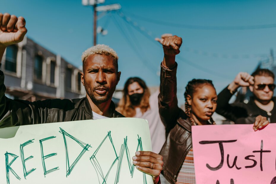 Diverse group of demonstrators with raised fists, one person holding a green 'FREEDOM' sign.