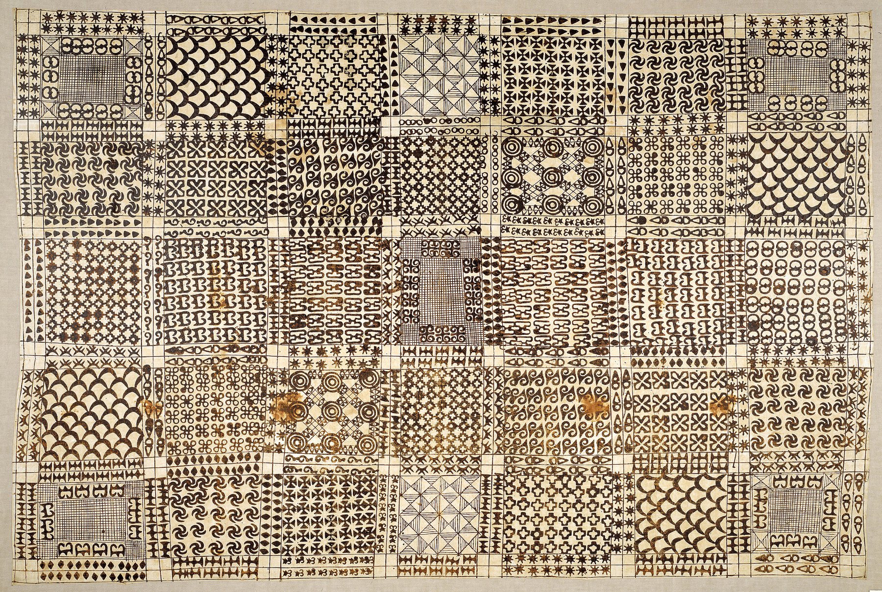White cloth wrapper with brownish black stamped patterns in thirty-five rectangular panels.
