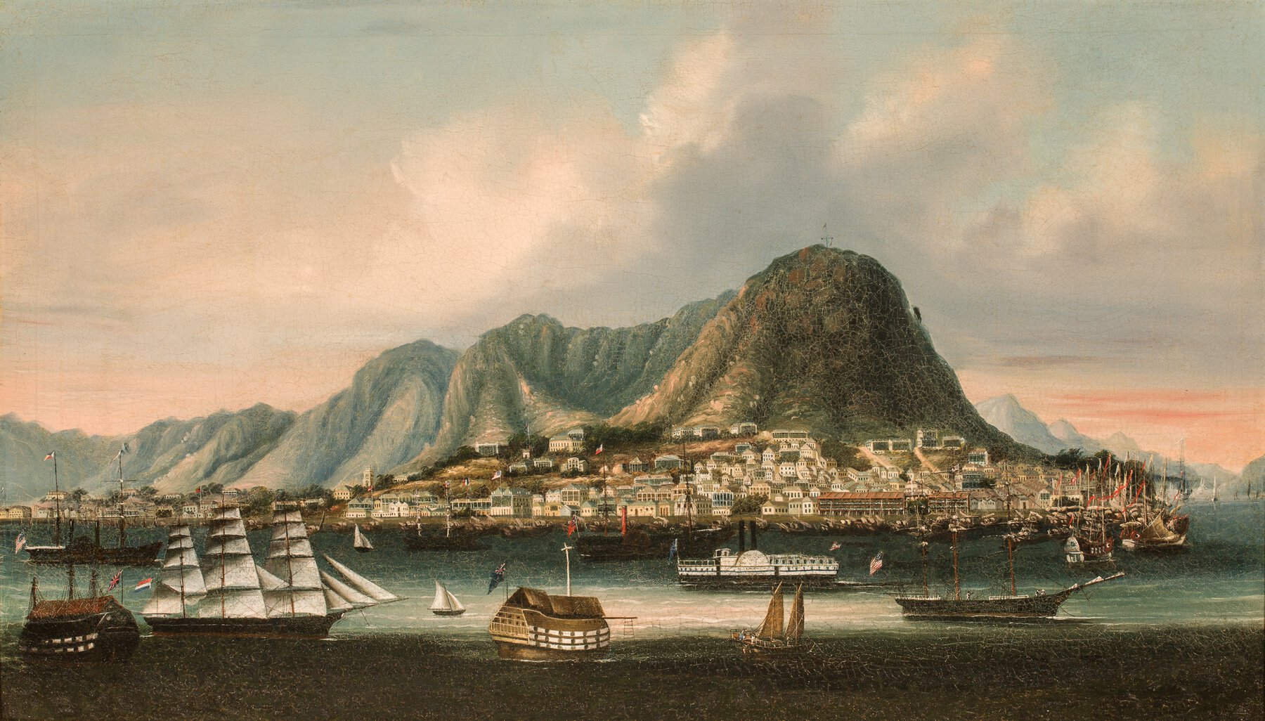 Harbour with steam and sailing ships in foreground, warehouses in background, mountains in distance.