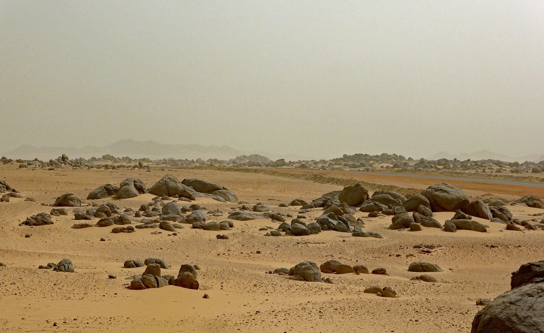 Nubian desert with sandy ground, big black rocks, and a gray sky.