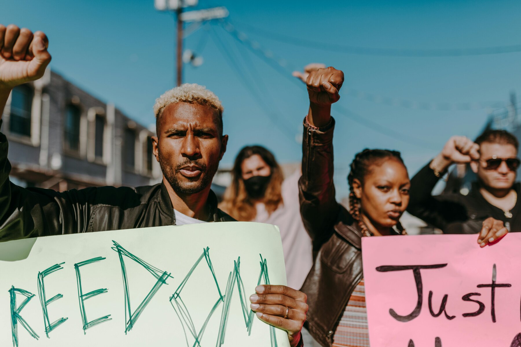 Diverse group of demonstrators with raised fists, one person holding a green 'FREEDOM' sign.
