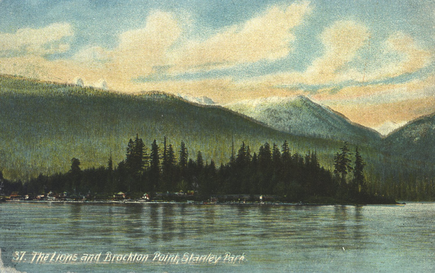 Small body of water with evergreen trees, green hills, and snow-capped mountains in distance.
