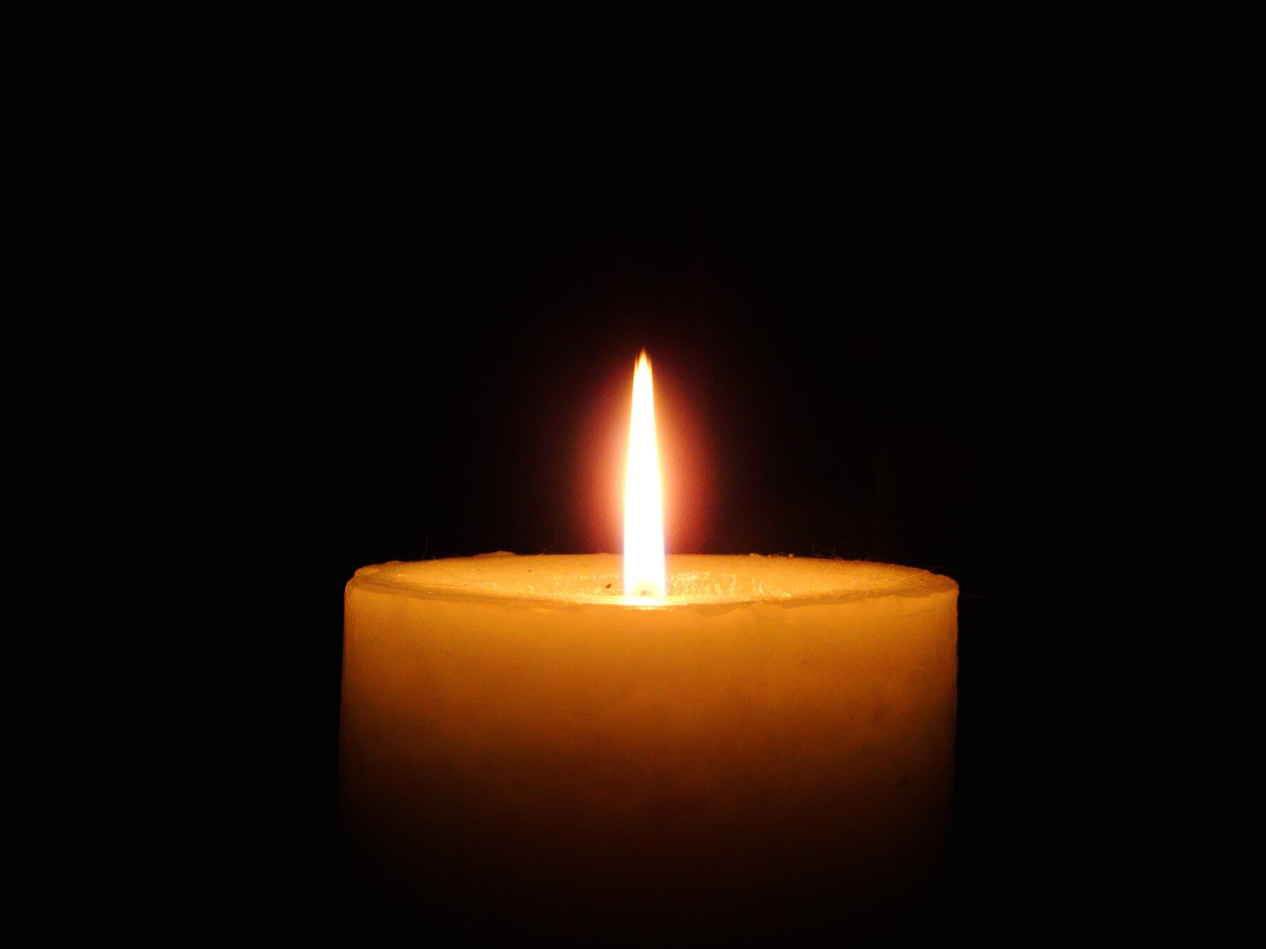 A burning orange candle against a black background.